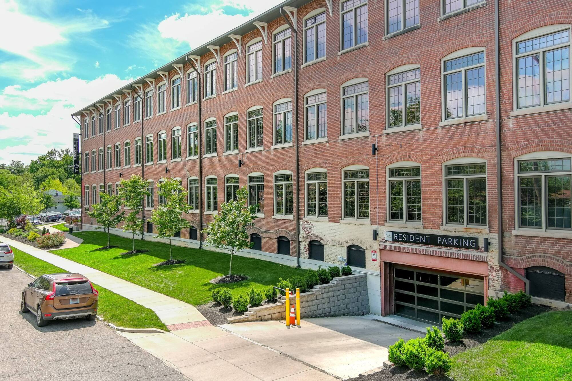 Red brick apartment building with large windows and a resident parking garage entrance on a sunny day.