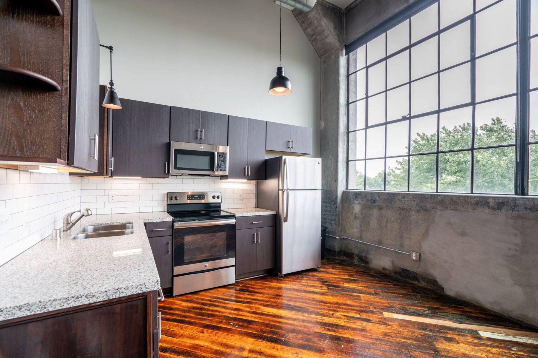 Empty room with wood floors, ceiling fan, and sliding glass door leading to a patio with vertical blinds at Apex West Midown.